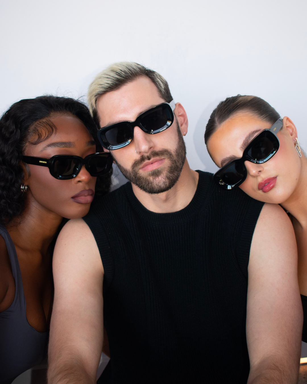 Image of three models with oval face shapes wearing our unisex Unfazed sunglasses. The sunglasses feature a sleek black rectangular frame and grey see-through lenses with TAC polarized and scratch-resistant coating. They provide full UV protection up to 500 nanometers, designed for universal fit and comfort.