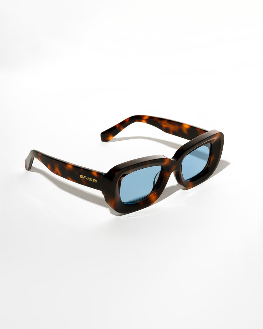 Side product shot of Rewrites tortoiseshell rectangular sunglasses: Handcrafted in Italy from 100% premium Mazzucchelli acetate, this side product shot showcases tortoiseshell rectangular sunglasses with a blue see-through TAC polarized lens for superior visual clarity and polarization. They include a scratch-resistant coating that blocks 100% harmful UV rays up to 400 nanometers. Highly impact-resistant and unisex, complete with our Rewrites logo in gold on the outside temples.
