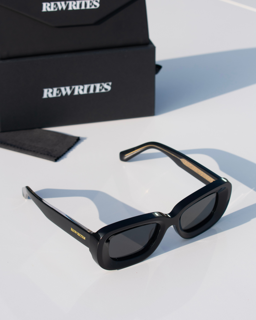 Front view of Rewrites Limited Edition Unfazed Sunglasses. Handcrafted in Italy from Mazzucchelli acetate, featuring a rectangular shape and sturdy fit. The unisex design includes thick black frames and grey see-through lenses with a scratch-resistant coating.