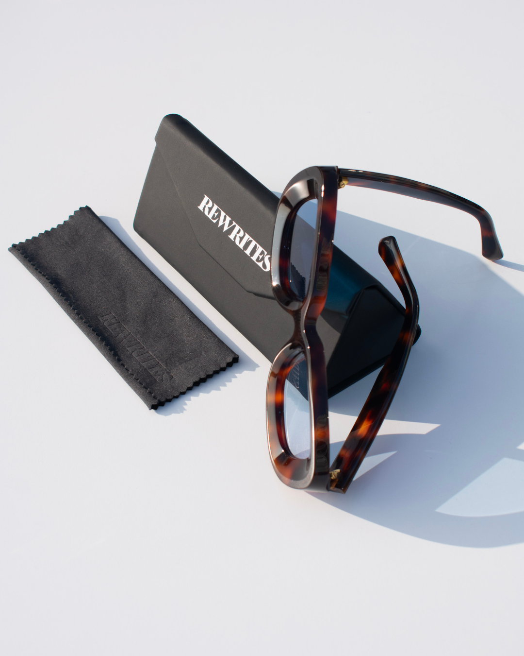 Front view of Rewrites Limited Edition Unfazed Sunglasses. Handcrafted in Italy from Mazzucchelli acetate, featuring a rectangular shape and sturdy fit. The unisex design includes thick tortoiseshell frames and blue see-through lenses with a scratch-resistant coating.